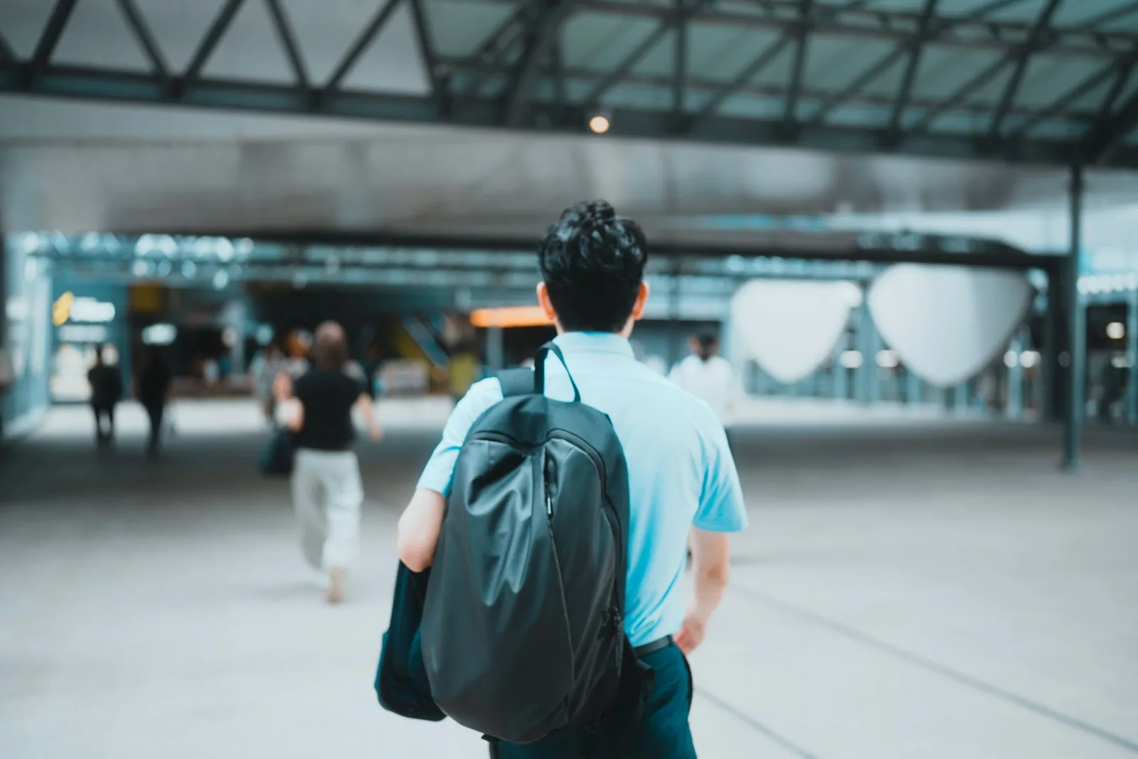 a traveler with a black backpack walking through a bright, modern transit hall